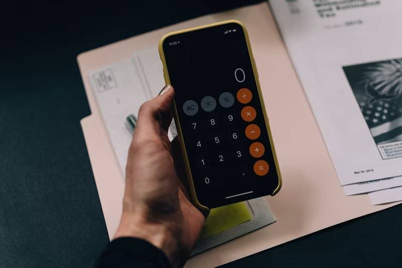 A drawing compass, ledger, desk clock and measuring tape arranged on a dark green desk — the four calculator families DailyCalc covers.